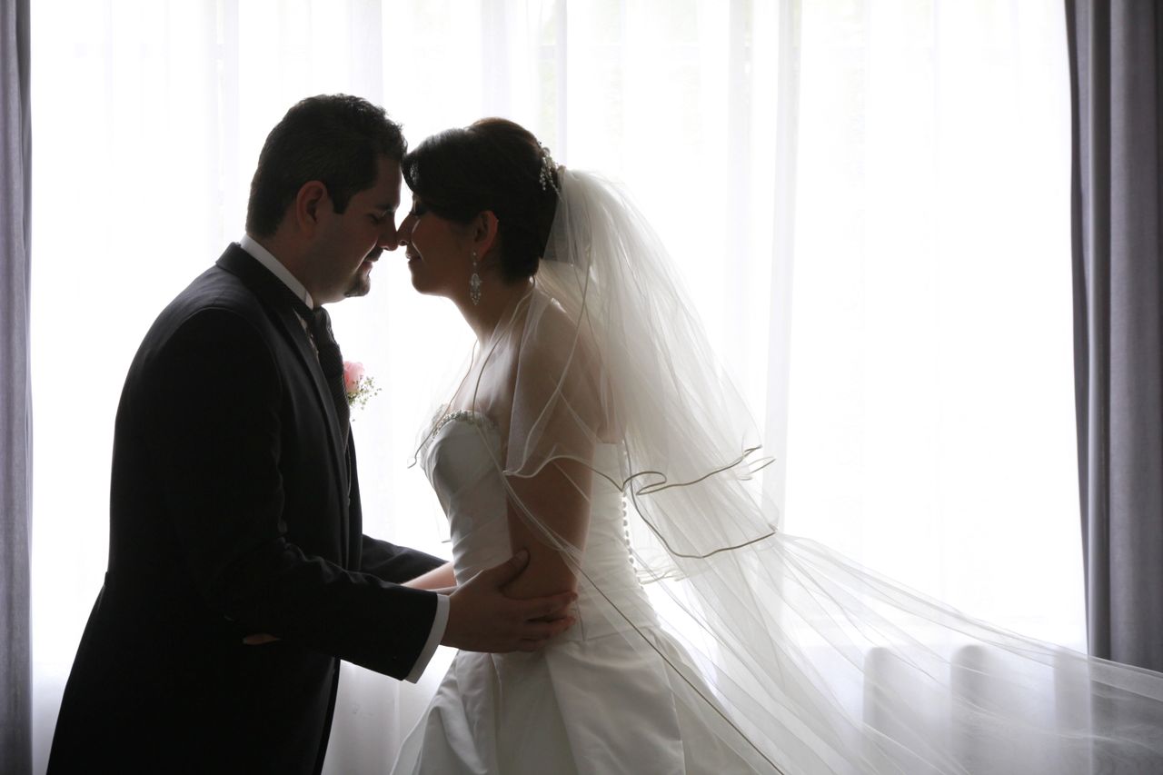 A loving bride and groom share an intimate moment by a large window.